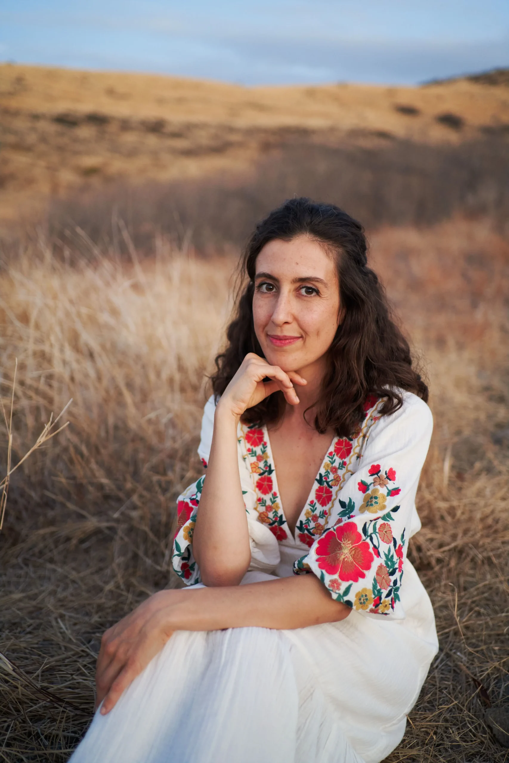 Silvia souriante pose en regardant de face, assise dans les herbes desséchées d'une prairie en plein été